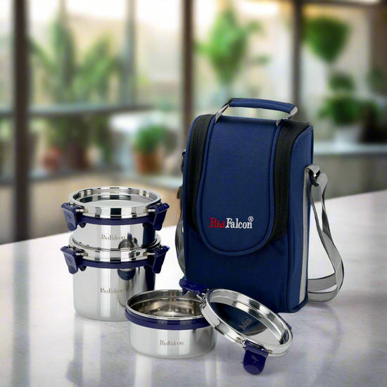 A set of three blue stainless steel lunch boxes with a blue insulated carrying bag and a stainless steel spoon. The lunch boxes have a locking mechanism and are displayed alongside the carrying bag which has a shoulder strap.